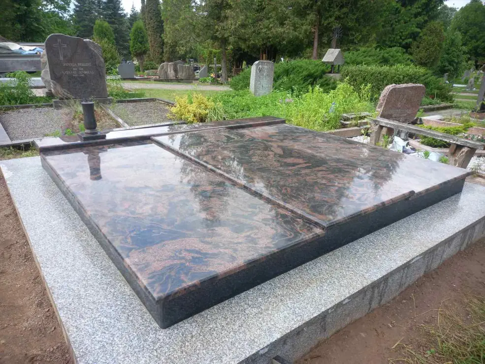 Rusvo granito kapavietės plokštės žalioje kapinių aplinkoje